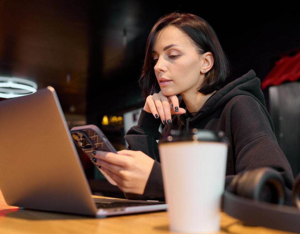 Brunetka trzymająca telefon, uśmiechnięta i zrelaksowana, w nowoczesnym otoczeniu.