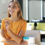 Kobieta trzymająca filiżankę, uśmiechająca się w biurze, symbolizująca pozytywne nastawienie w poszukiwaniu pracy.