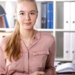 Kobieta uśmiechnięta siedzi przed komputerem, poszukując pracy w biurze.
