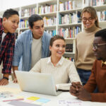 Grupa ludzi w sali lekcyjnej patrzy na laptopa, poszukując informacji o pracy. CV na staż
