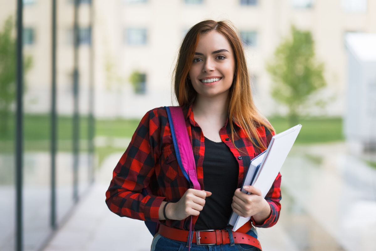 CV studenckie. Kobieta uśmiechnięta trzymająca książkę na świeżym powietrzu, symbolizująca poszukiwanie pracy.
